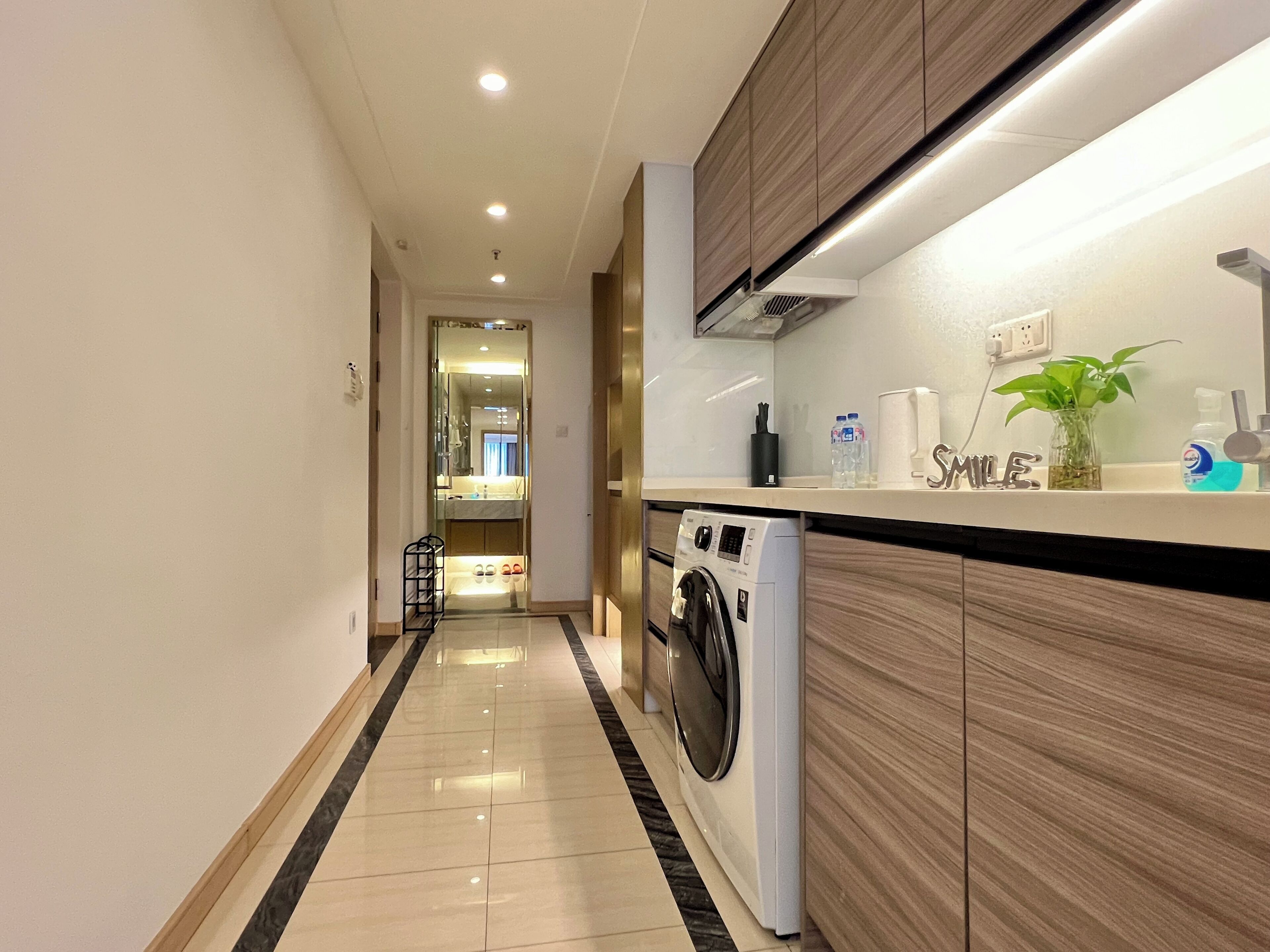 A modern kitchen with a built-in washing machine, a countertop with a plant, and a mirror reflecting the room.