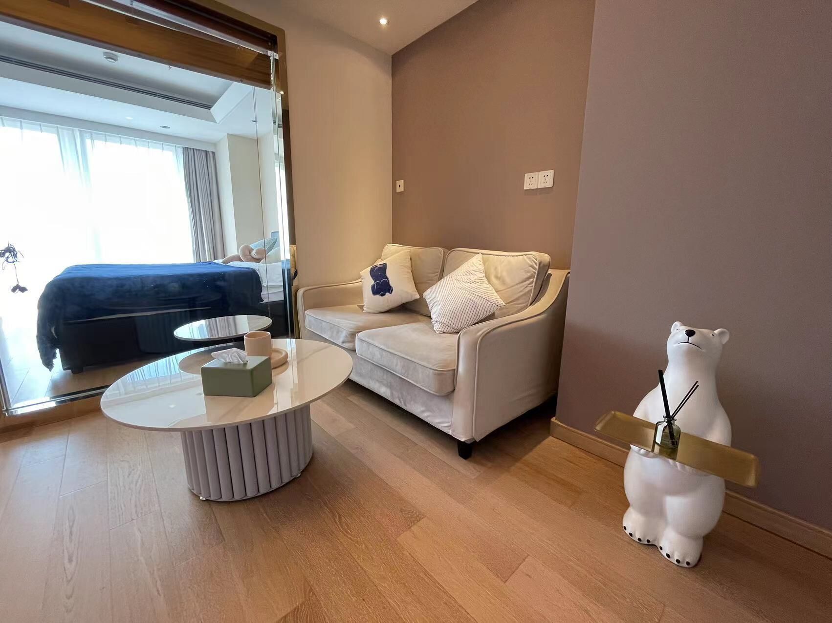 A modern hotel room with a sofa, a round coffee table, and a decorative bear statue.