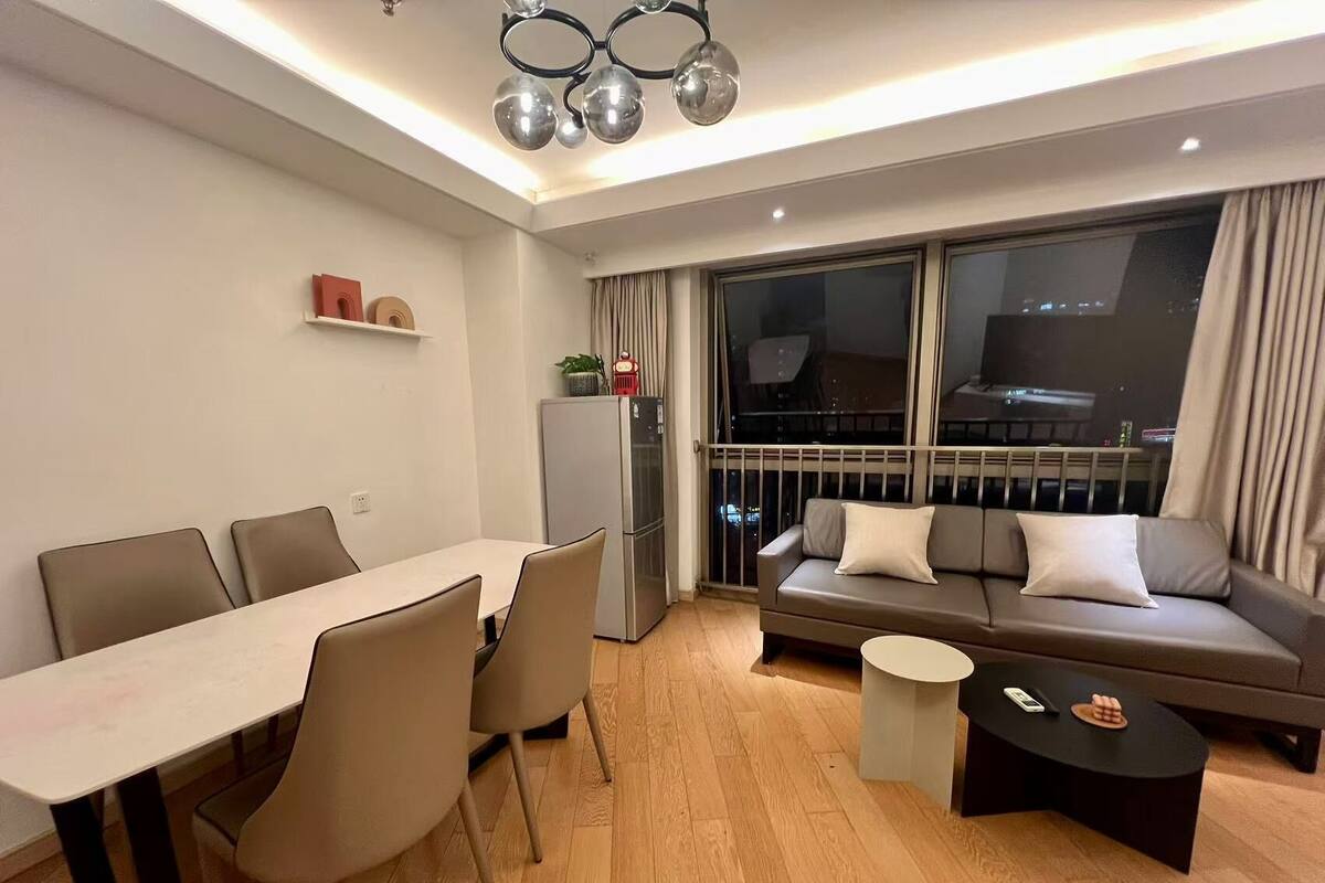 Un salon moderne comprenant un coin repas, un canapé, une petite table basse et un balcon offrant une vue sur la ville la nuit.