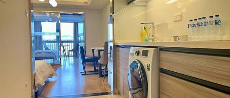 A modern hotel room with a washing machine, a dining area, and a balcony with a view.