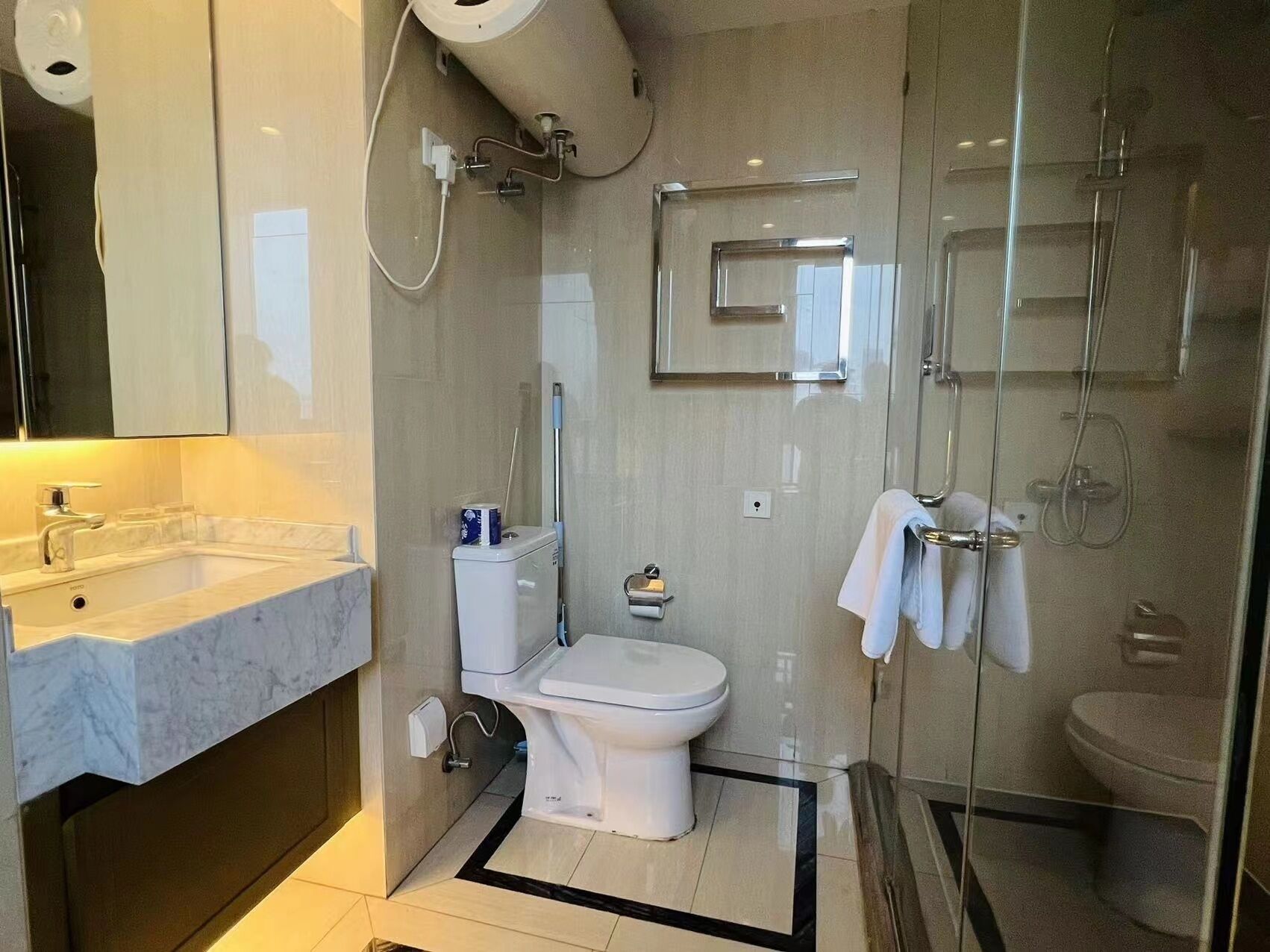 Une salle de bain moderne avec un lavabo en marbre, des toilettes, une douche en verre et un porte-serviettes.