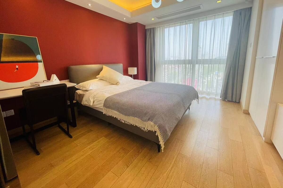 Une chambre d’hôtel avec un lit, un bureau, une chaise, un tableau au mur et une grande fenêtre avec des rideaux.