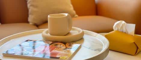 A round table with a magazine, a white mug, and a yellow tissue box.
