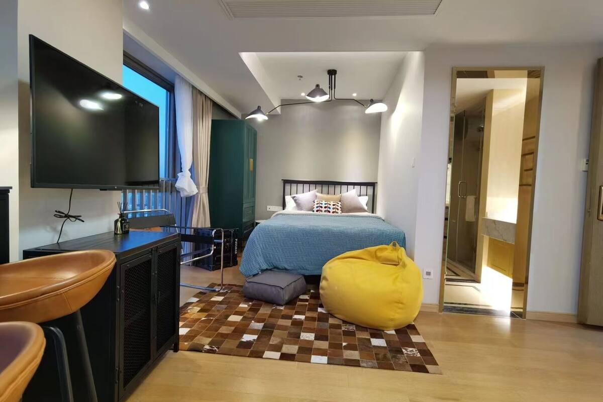 Une chambre à coucher moderne, équipée d’un lit, d’un bureau, d’une chaise, d’un téléviseur et d’un fauteuil poire.