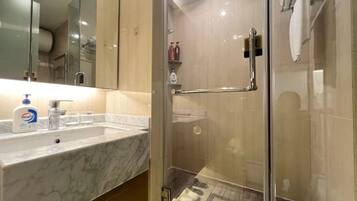 A modern bathroom with a glass shower enclosure, a marble sink, and toiletries on the counter.
