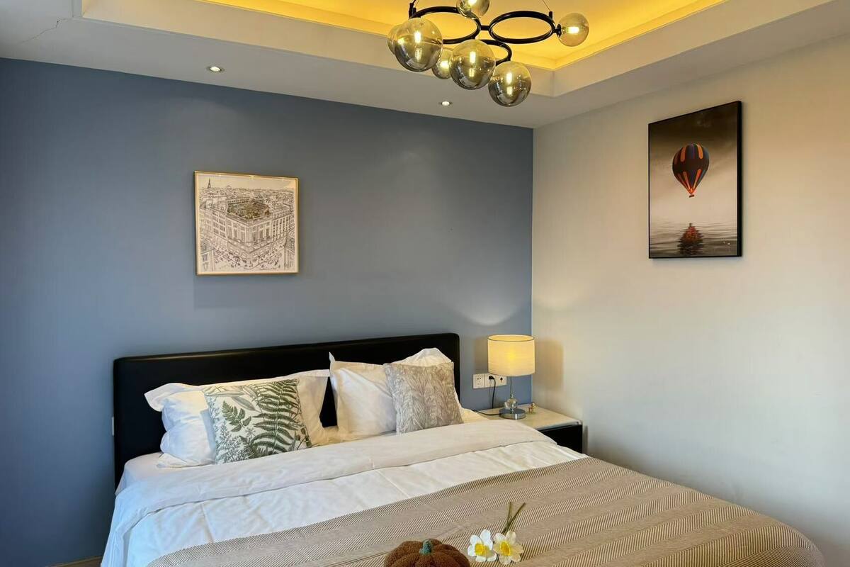 Une chambre à coucher moderne avec un grand lit, une table de chevet avec une lampe et des œuvres d’art accrochées aux murs.