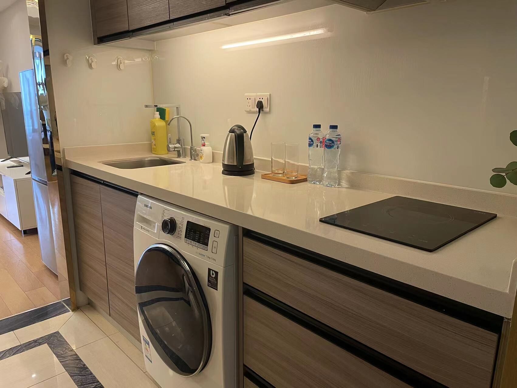 A modern kitchen with a built-in washer and dryer, a sink, a kettle, and a tablet on the counter.