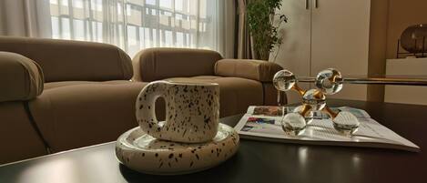 A modern living room with a leather sofa, a coffee table with a ceramic mug and decorative glass, and a magazine.