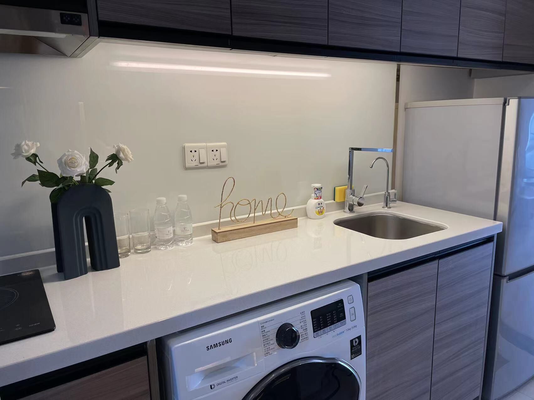 A modern kitchen with a built-in washing machine, a sink, and a countertop with a vase of white roses.