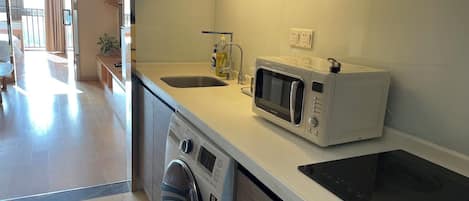 A modern kitchen with a built-in microwave, a toaster, a washing machine, and a sink.
