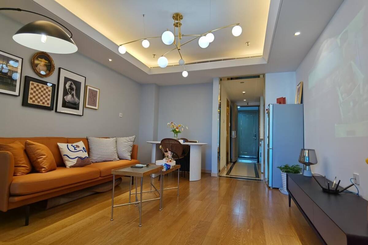 Un salon moderne avec un canapé, une table basse et un coin repas. On y trouve un luminaire au plafond et des tableaux encadrés accrochés au mur.