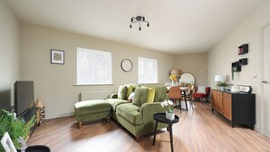 Una sala de estar con un sofá verde, una mesa de comedor con sillas, un mueble negro y una pequeña mesita con una planta.