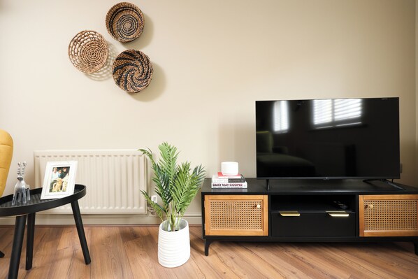 A living room with a black TV stand, a white radiator, and a potted plant. - Stylish Flat With Sofa Bed in Malmesbury (Malmesbury)