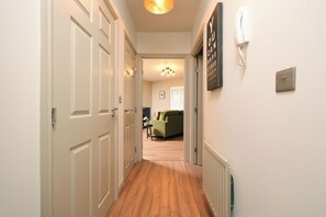 A hallway with wooden flooring, white doors, a wall-mounted telephone, and a radiator. - Stylish Flat With Sofa Bed in Malmesbury (Malmesbury)