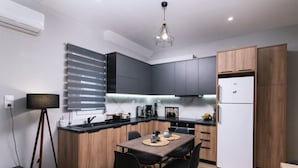 Eine moderne Küche mit dunklen Schränken, einem weißen Kühlschrank und einem Essbereich mit einem Holztisch und schwarzen Stühlen.
