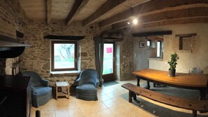 A rustic room with stone walls, a wooden bench, two armchairs, a small table, and a potted plant. - Farm cottage (Sainte-Christine)