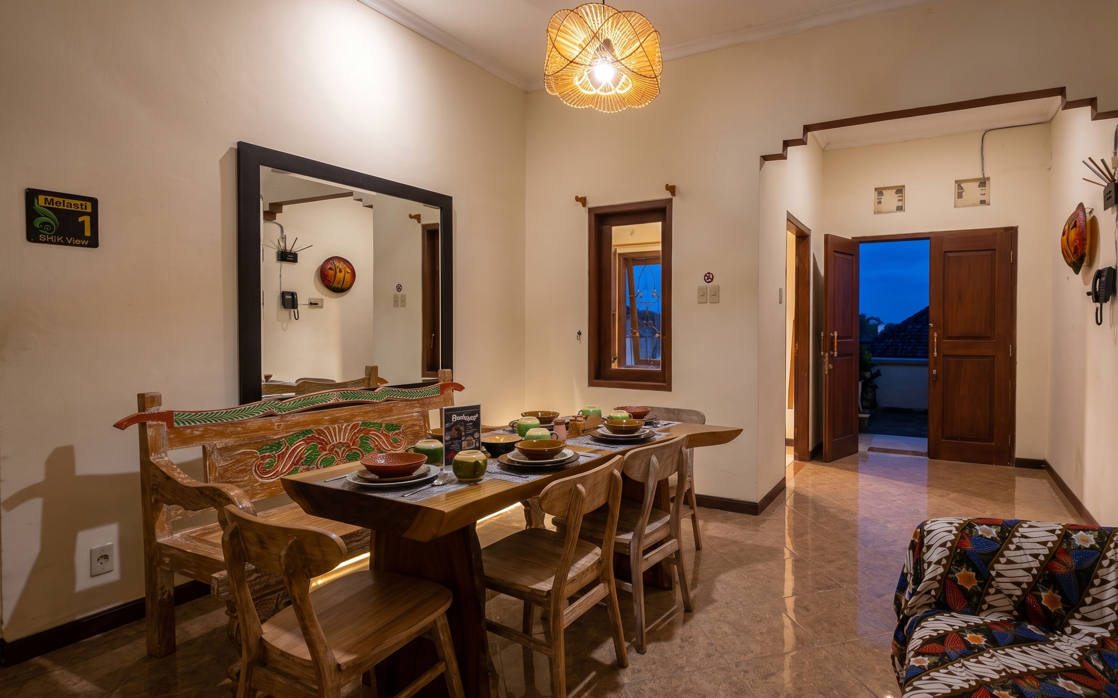 A dining area with a wooden table and chairs, a large mirror, and a view of the outside.