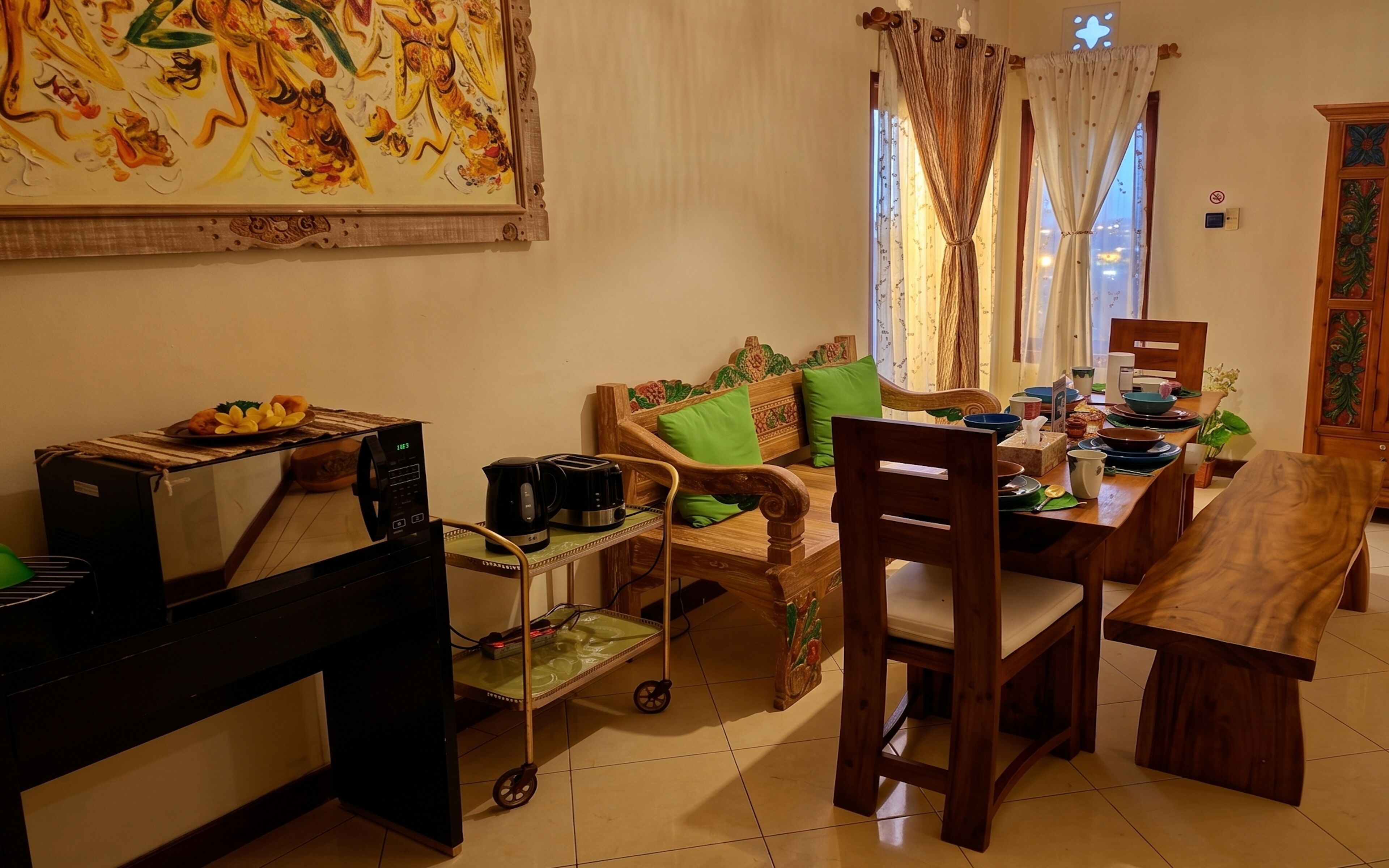 A living room with a sofa, dining table, chairs, a coffee machine, a cart, and a painting on the wall.