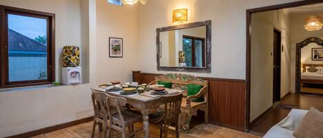 Un comedor con una mesa preparada para cuatro, un sofá, un espejo y una ventana con vista a una casa.