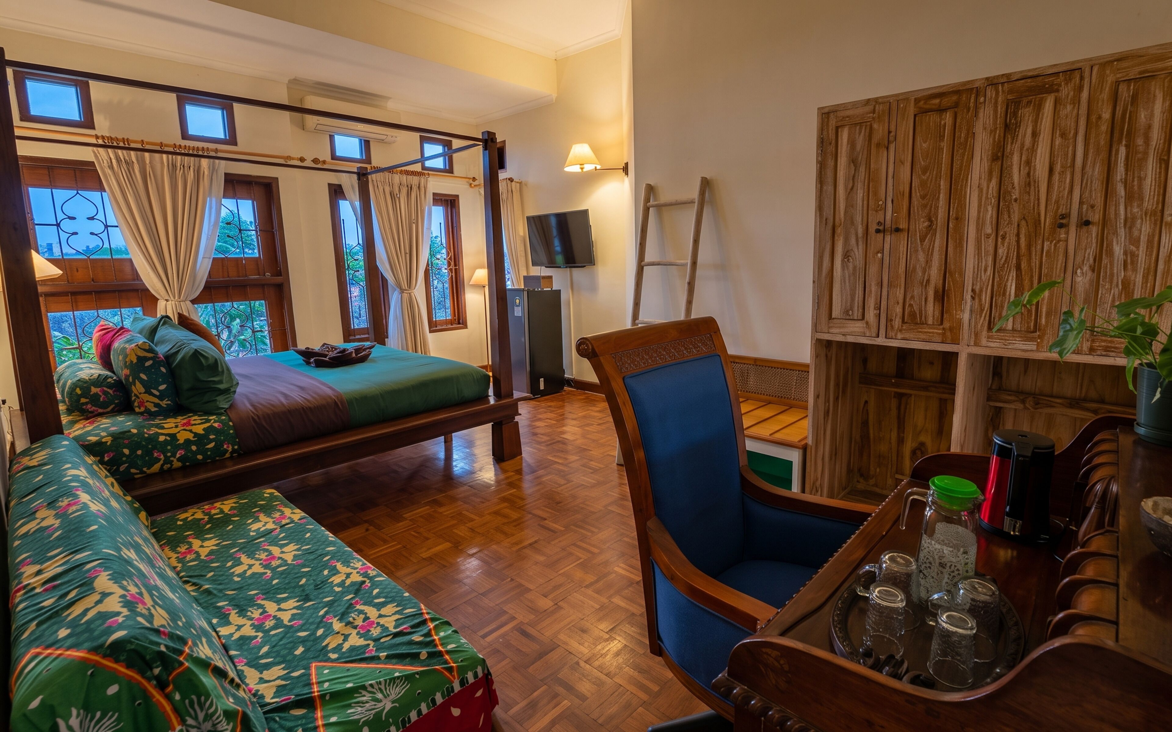 A room with a bed, a sofa, a TV, a wooden cabinet, and a tray with glasses.