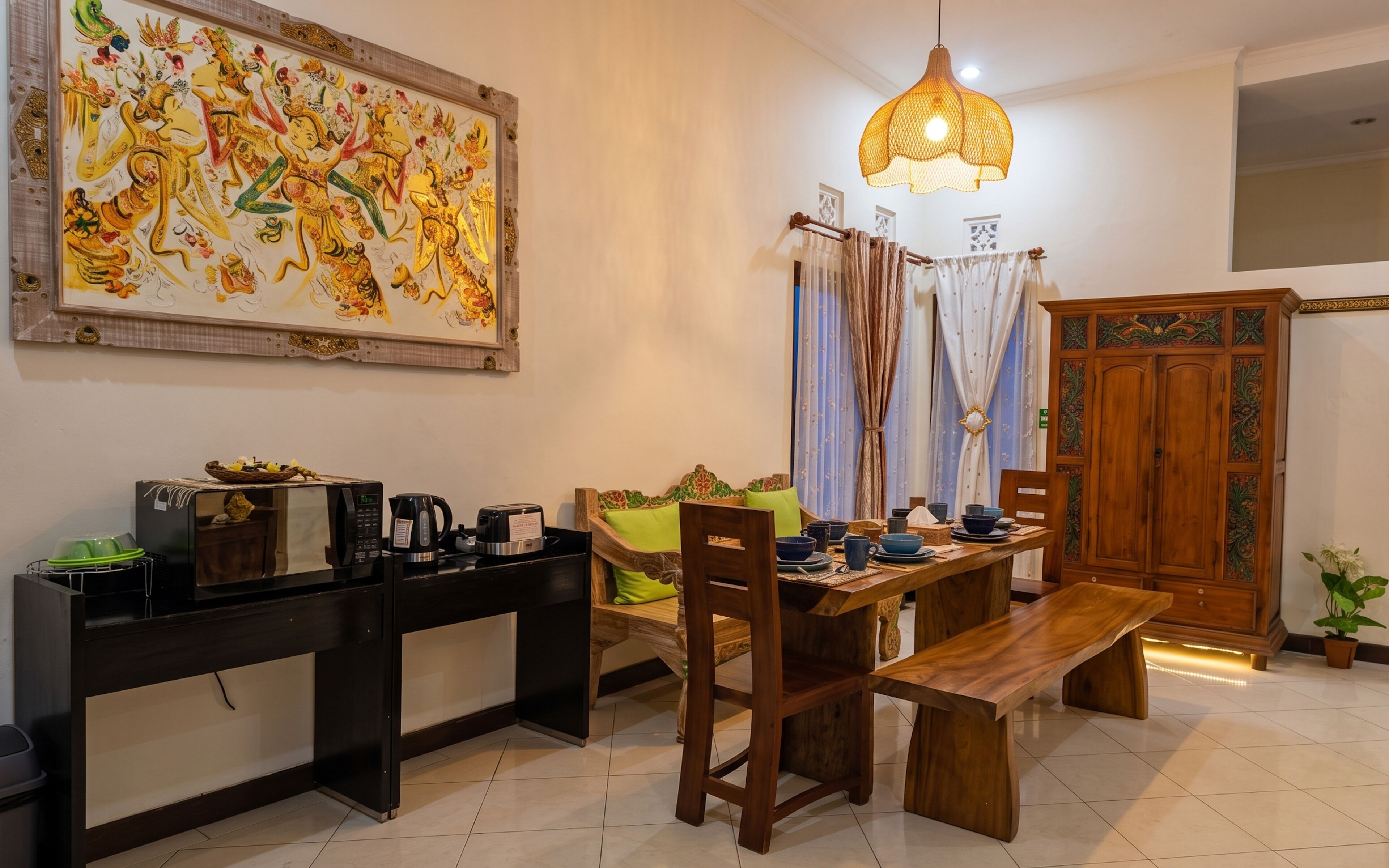 A dining area with a wooden table, chairs, a bench, a decorative painting, a cabinet, and a hanging light fixture.