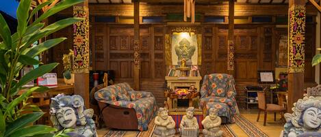 Una habitación con techo de madera, un candelabro, una estatua de Buda, un sofá y un tapete estampado.