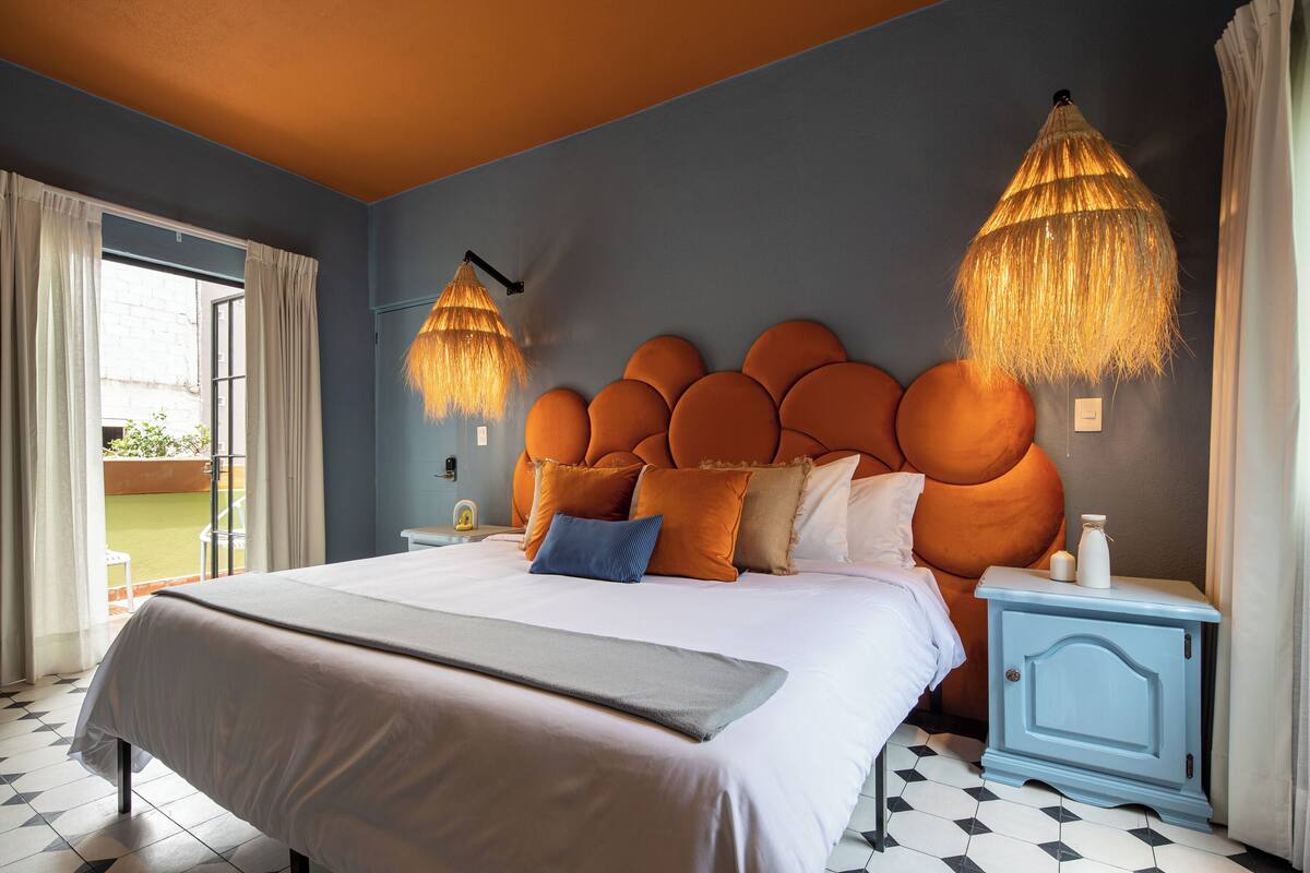 Ein Schlafzimmer mit einem großen Bett, einem auffälligen orangefarbenen Kopfteil und zwei Pendelleuchten.