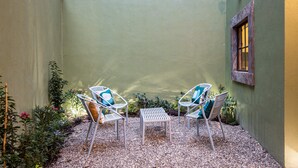 A courtyard with two white metal chairs, a small table, and a wall covered in green ivy.
