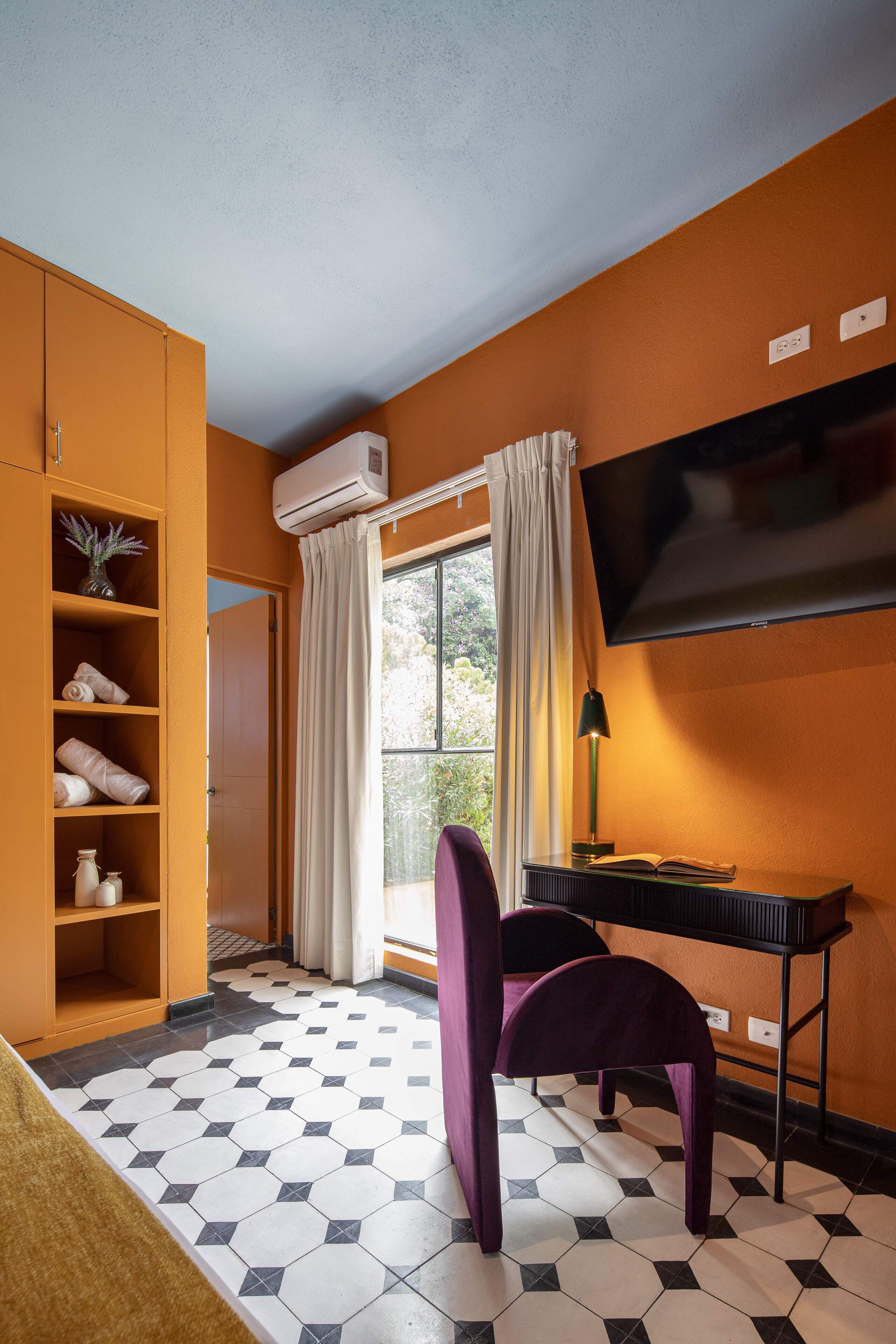 A room with a tiled floor, a TV mounted on the wall, a desk with a lamp, and a chair.