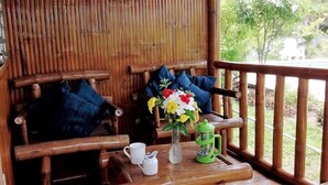 Een houten terras met een bankje, een tafel met een bloevas, een mok en een groene koffiepers.