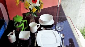 Een gedekte tafel met witte borden, een groene koffiepot en een vaas met bloemen.