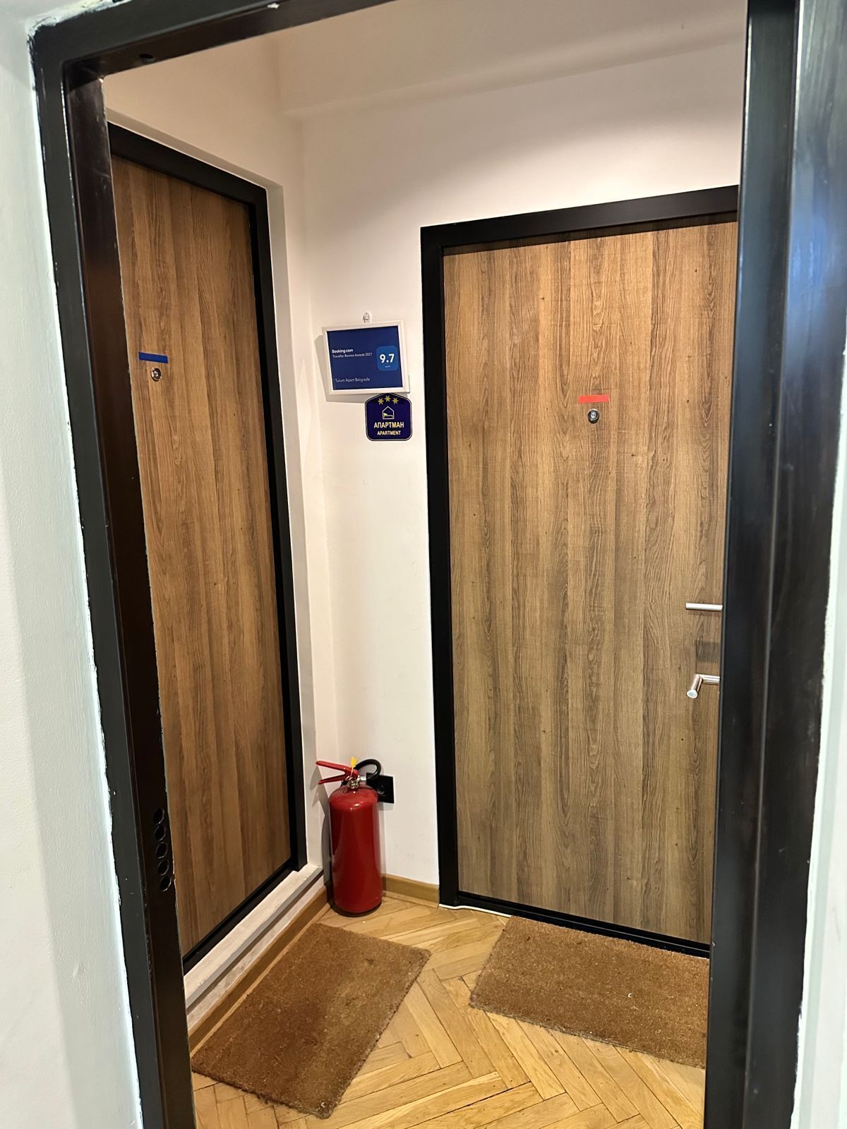 Un pasillo con dos puertas de madera, un extintor y un cartel que indica una calificación de 9.7.