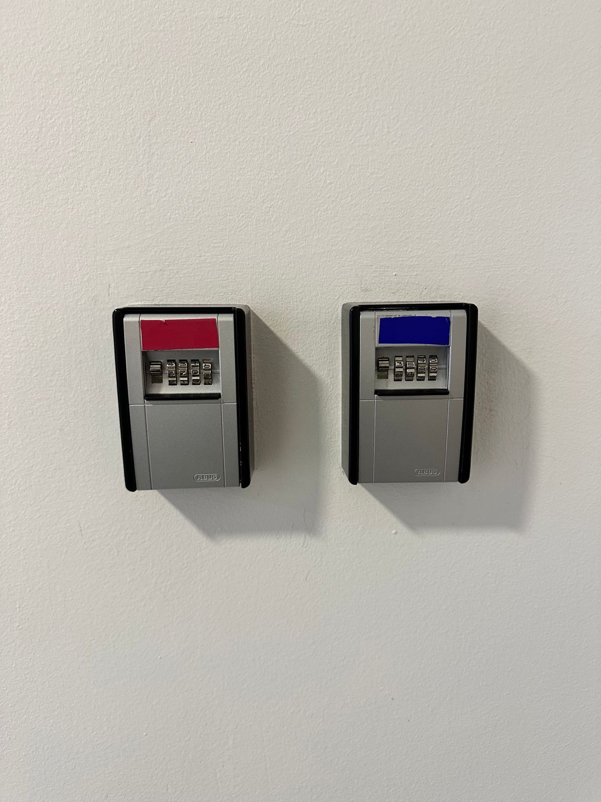 Two wall-mounted intercoms, one red and one blue, on a plain white wall.