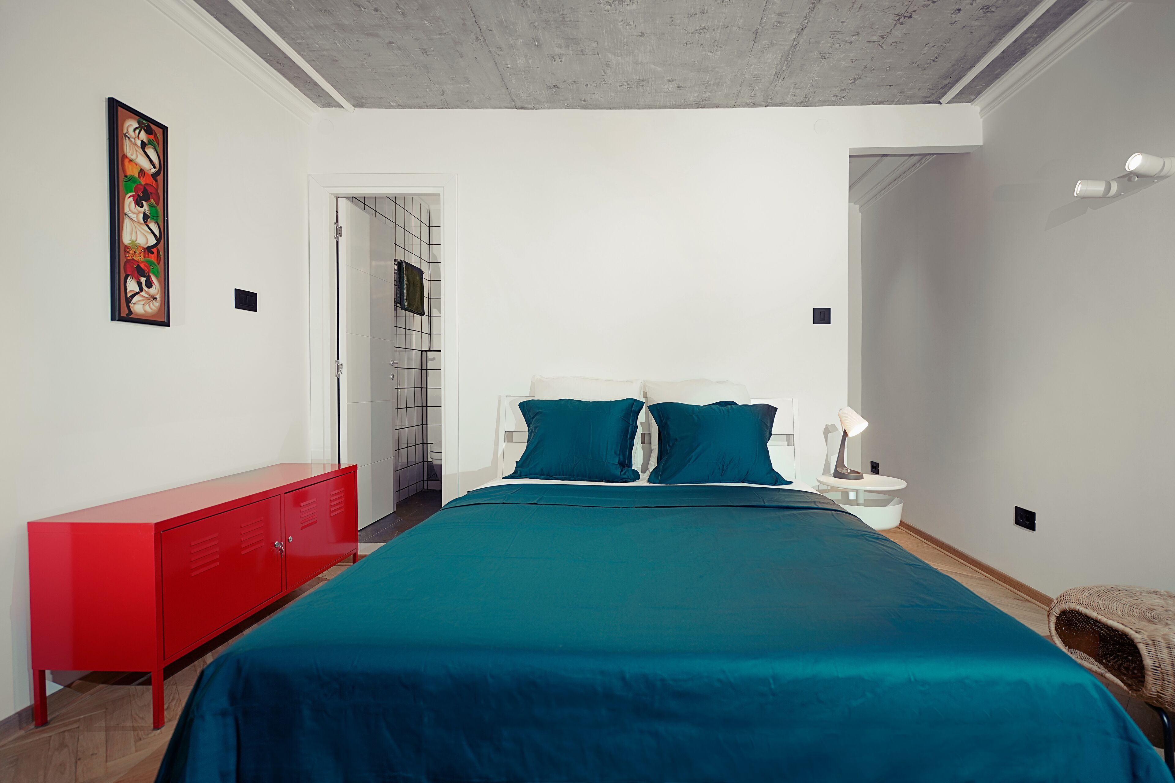 Une chambre à coucher avec un grand lit, une commode rouge, une table de chevet blanche et une lampe fixée au mur.
