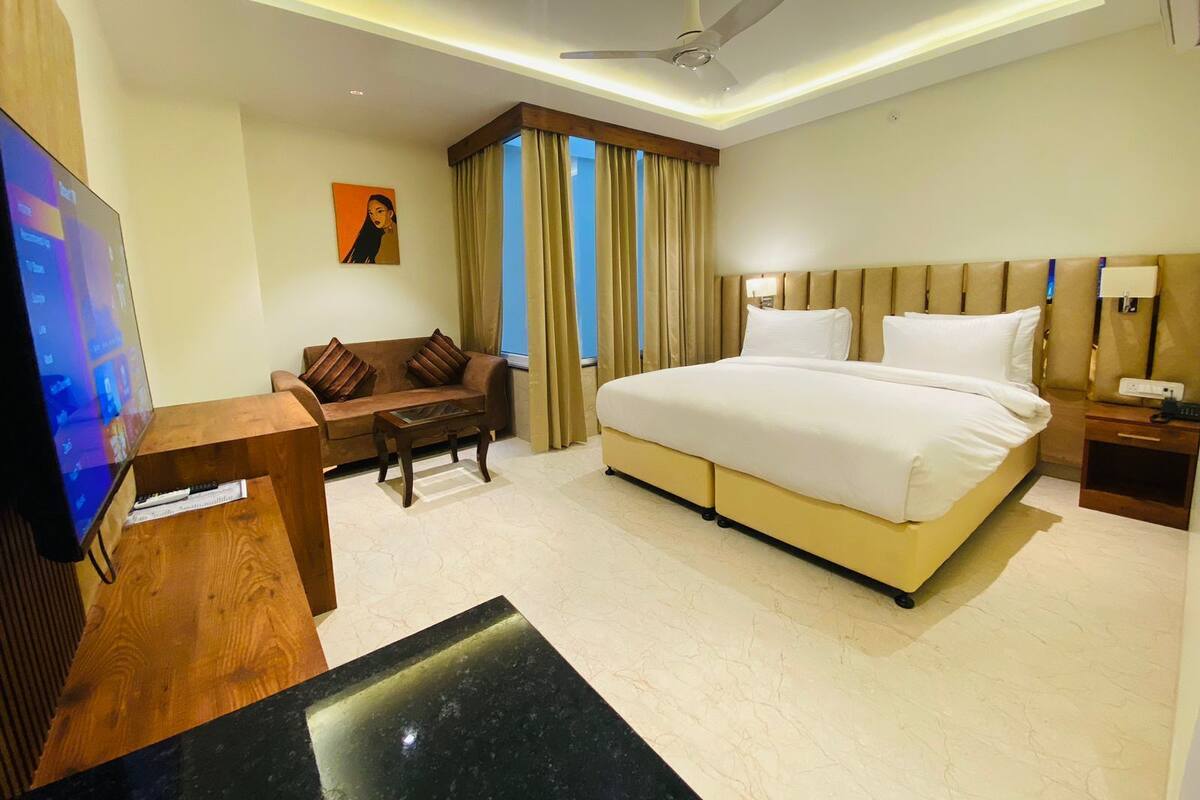 Una habitación de hotel con cama, sofá, televisor, ventilador de techo y cortinas.