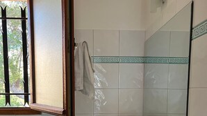 A bathroom with white tiles, a wooden shelf with folded towels, a towel rack, and a window with a view of trees. - Chambre Dhôte 2 Personnes à la Panouse, Marseille 13009 (Marseille)