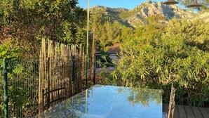 A glass-top table with metal legs on a wooden deck, surrounded by bamboo fencing and greenery, with a mountainous backdrop. - Chambre Dhôte 2 Personnes à la Panouse, Marseille 13009 (Marseille)