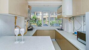 A modern kitchen with white countertops, beige cabinets, and a window providing a view of the outside. - Qingdao Little Times Youth Hostel May4th Square Store (Qingdao)