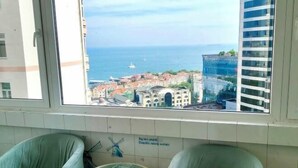A room with two green chairs, a small round table, and a view of a coastal cityscape through a window. - Qingdao Little Times Youth Hostel May4th Square Store (Qingdao)