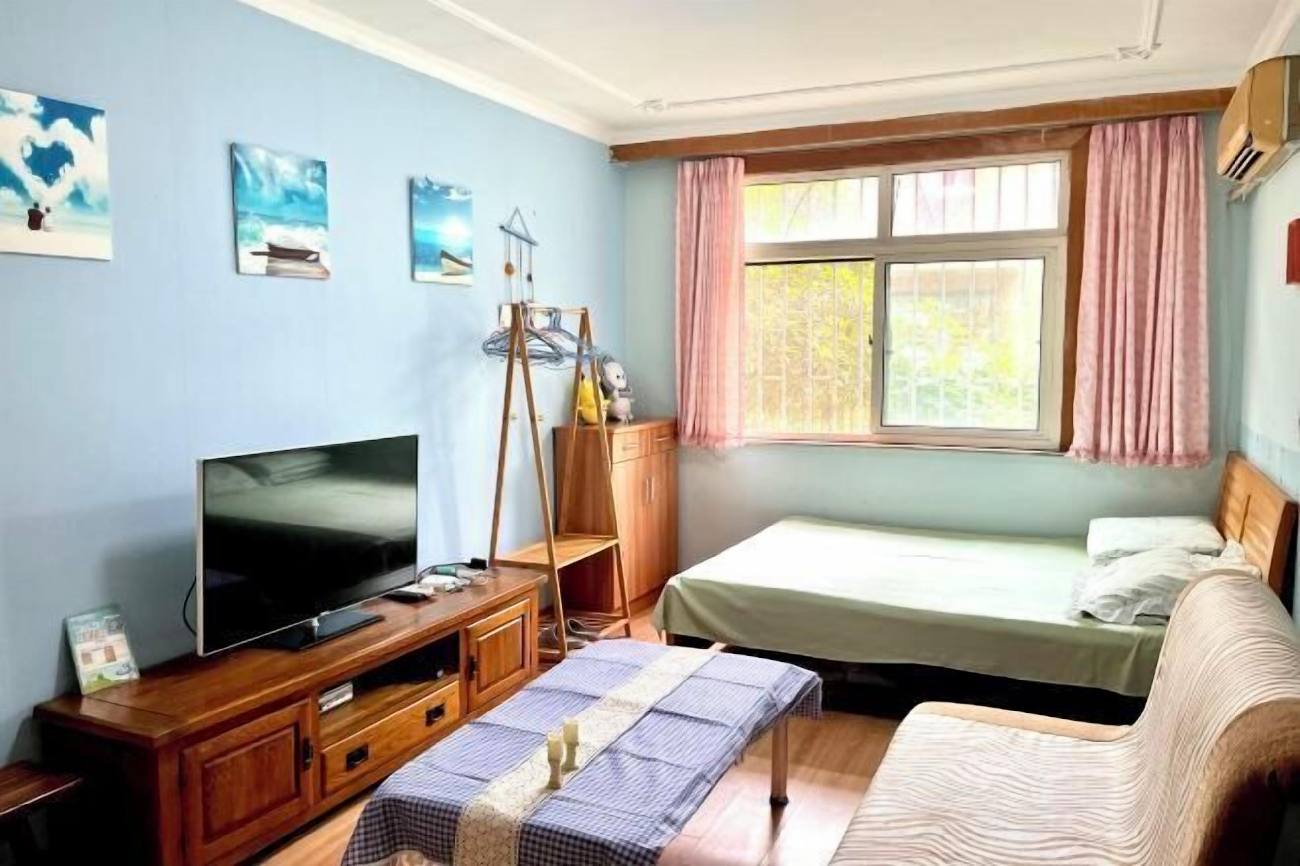 A bedroom with a bed, a TV, a wooden cabinet, and a window with curtains.