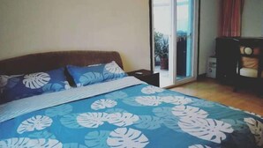 A bedroom with a bed, a nightstand, a chair, and a sliding glass door leading to a balcony. - Qingdao Little Times Youth Hostel May4th Square Store (Qingdao)
