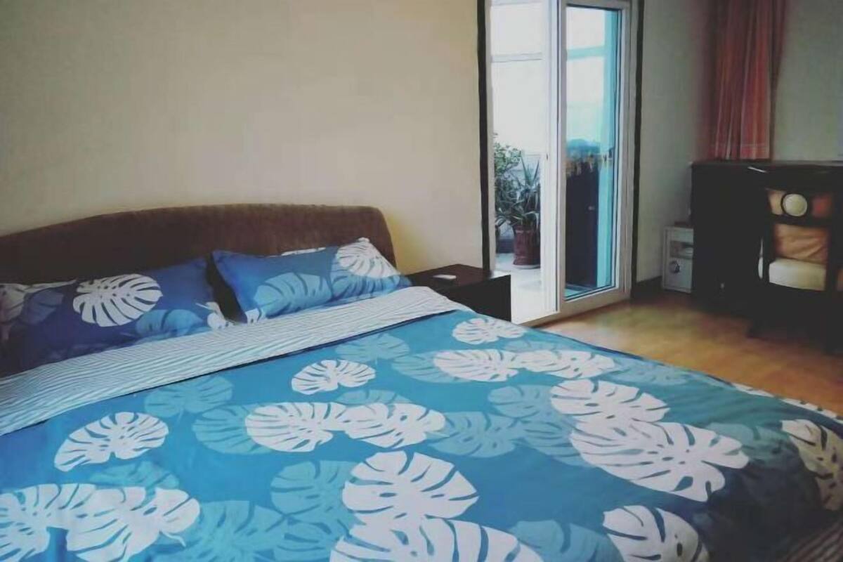 Een slaapkamer met een bed, een nachtkastje, een stoel en een schuifdeur naar een balkon.