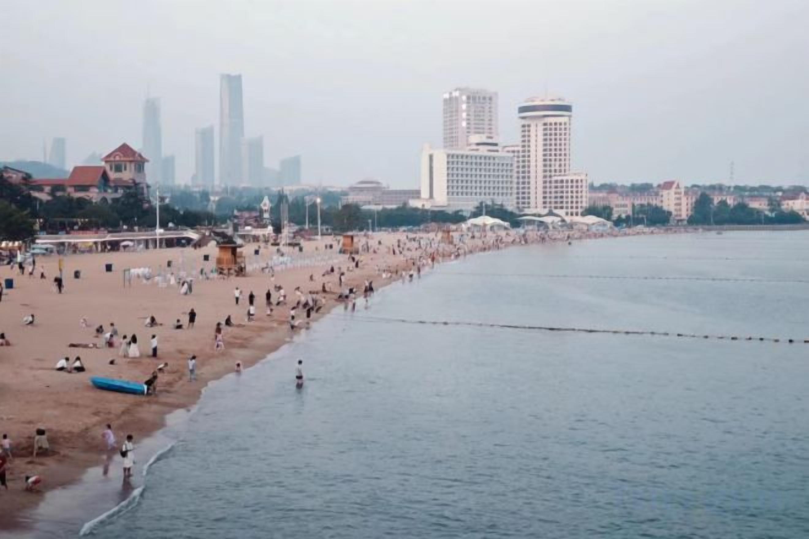Una playa con una larga extensión de arena y un mar tranquilo, con edificios al fondo.