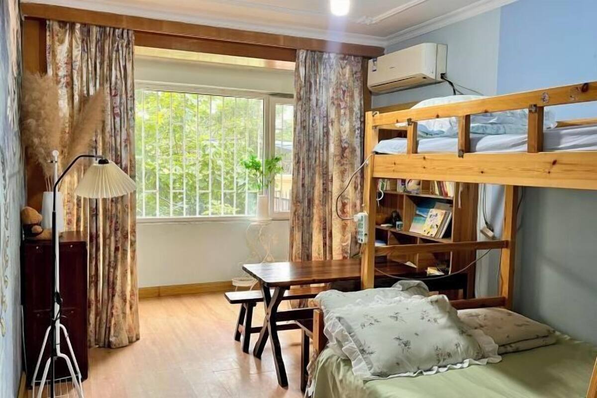 Een kamer met een stapelbed, een bureau, een lamp, een raam met gordijnen en een airconditioning.