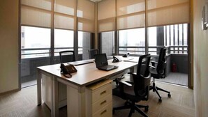 Un espacio de oficina moderno con un escritorio grande, sillas y ventanas amplias con persianas.