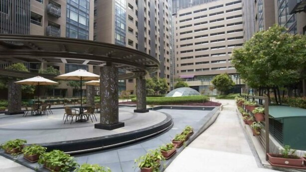 Un patio con mesas al aire libre, plantas en macetas y edificios modernos al fondo.