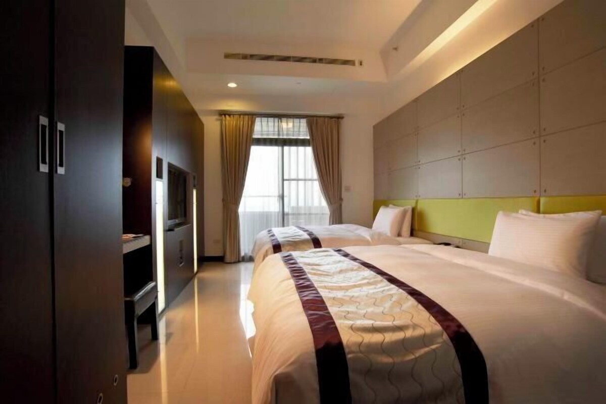 A hotel room with two beds, a television, a flat-screen TV, and a large window with curtains.