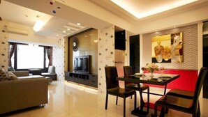 Una sala moderna con un sofá, una mesa de comedor con sillas, un televisor y una pared decorativa roja.
