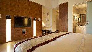 Una habitación de hotel moderna con una cama grande, un televisor de pantalla plana montado en la pared, un revestimiento de pared de madera y un baño visible a través de una puerta abierta.