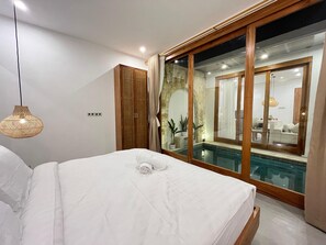 Ein Schlafzimmer mit einem Bett, einem Holzschrank, einer Glastür zu einem Poolbereich und einer Hängeleuchte.
